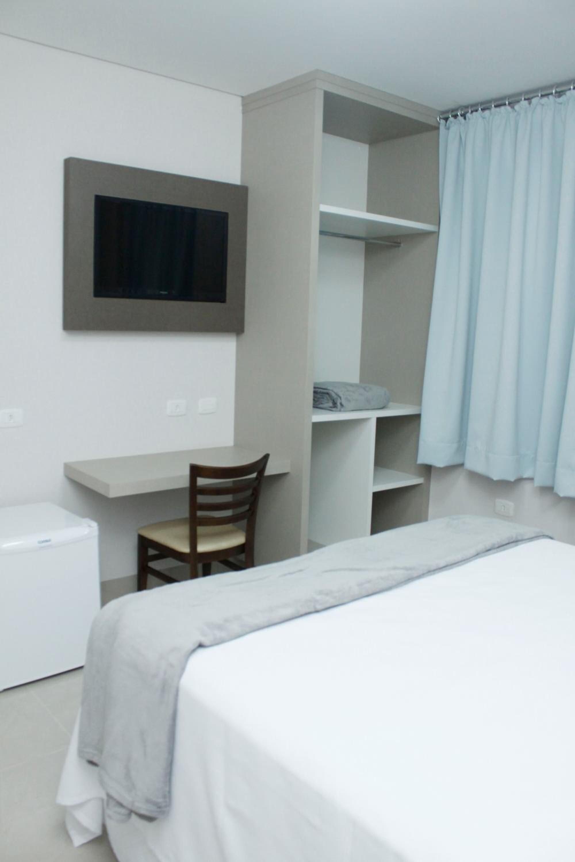 A bedroom with a bed, a desk, a chair, a television, and a wardrobe.
