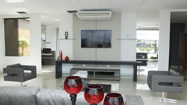 A modern living room with a grey sofa, a flat-screen TV mounted on the wall, and a minimalist design. - Hotel Cadori (Paicandu)