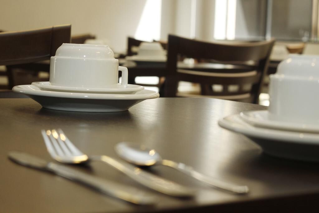 A dining table with a white cup and saucer, a fork, and a knife.