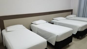 Quarto de hotel com três camas individuais, cada uma com roupa de cama branca e um travesseiro.