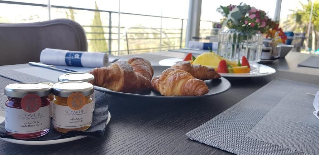 A breakfast setting with croissants, fruit, and jars of jam on a table.