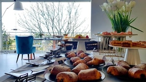 A breakfast buffet with pastries and fruits, a blue chair, and a view of trees through large windows. - Hotel Villa Flora Relais (Caltanissetta)