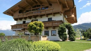 Una cabaña de madera de varios pisos con balcones, rodeada de exuberante vegetación y montañas al fondo.