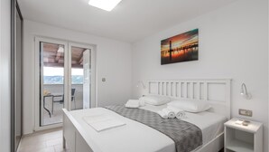 A bedroom with a bed, a bedside table, a nightstand, a window with blinds, and a painting on the wall. - Beach front home in Lopar (Lopar)