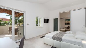 A modern bedroom with a bed, a desk, and a chair. There is a sliding glass door leading to an outdoor area with a table and chairs. - Beach front home in Lopar (Lopar)