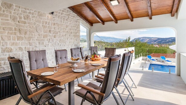 A dining area with a stone wall, wooden ceiling, and a view of mountains and a pool. - Beach front home in Lopar (Lopar)