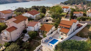 A coastal residential area with houses featuring red-tiled roofs, a swimming pool, and a view of the sea. - Beach front home in Lopar (Lopar)