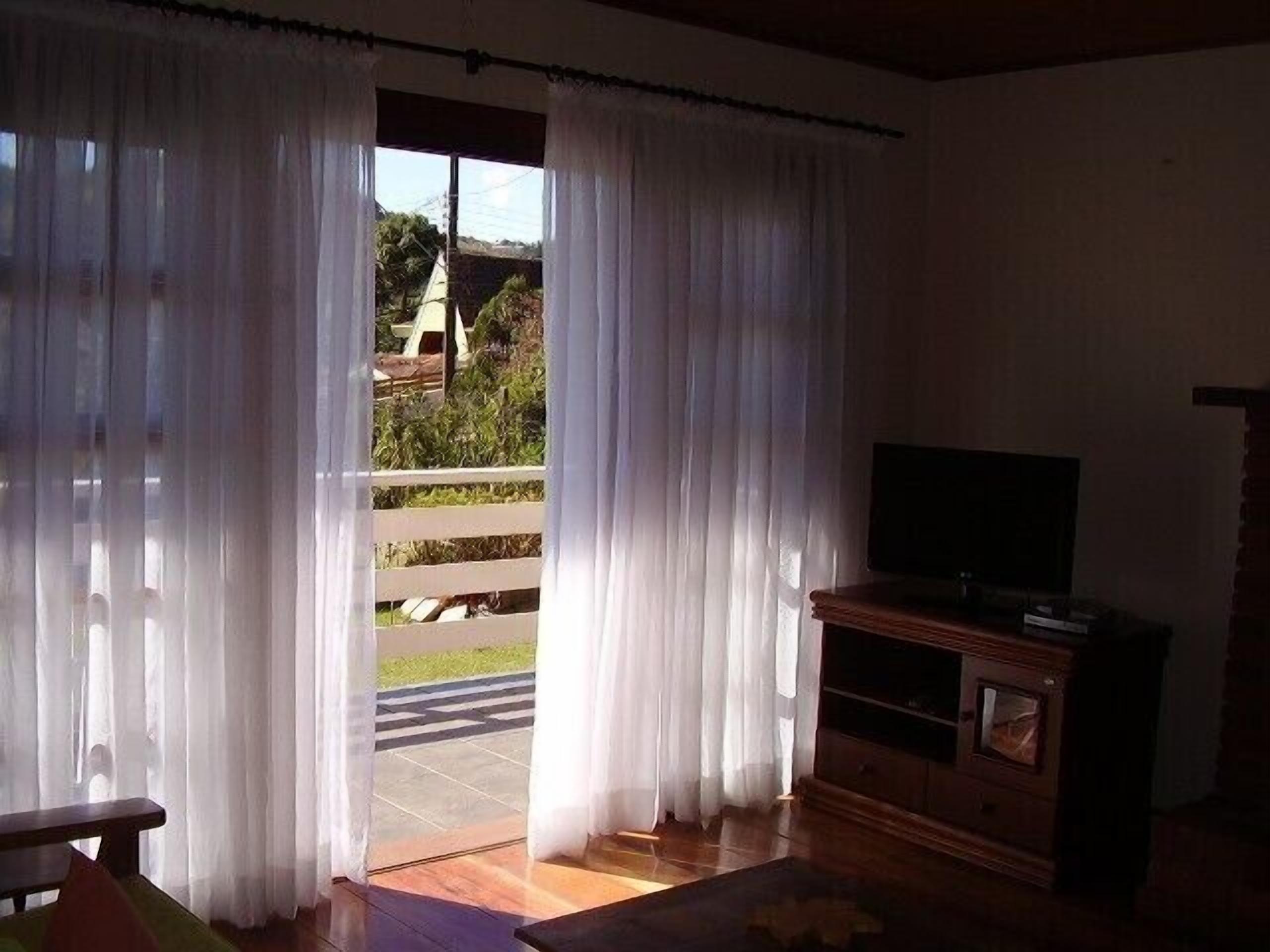 A room with a wooden bench, a television on a wooden stand, and a sliding glass door with white curtains.
