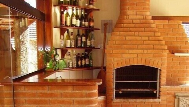 A brick fireplace with a pizza oven, a bar area with shelves of bottles, and a tiled floor.