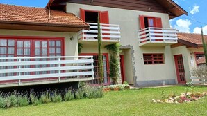 A two-story building with a red-tiled roof, balconies with white railings, and a small garden area with flowers and shrubs.