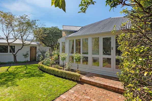 A house with a conservatory, a well-maintained lawn, and a brick pathway leading to the entrance.
