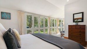 Un dormitorio con una cama grande, un aparador de madera y vistas al exterior a través de amplios ventanales.