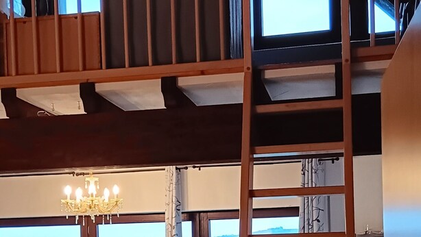 A dining area with a table and chairs, a wooden ladder, and a view of the outdoors.