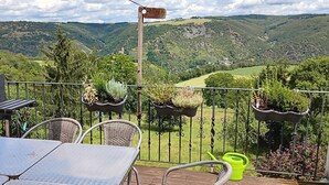 A balcony with a table and chairs, a grill, and hanging planters with greenery.