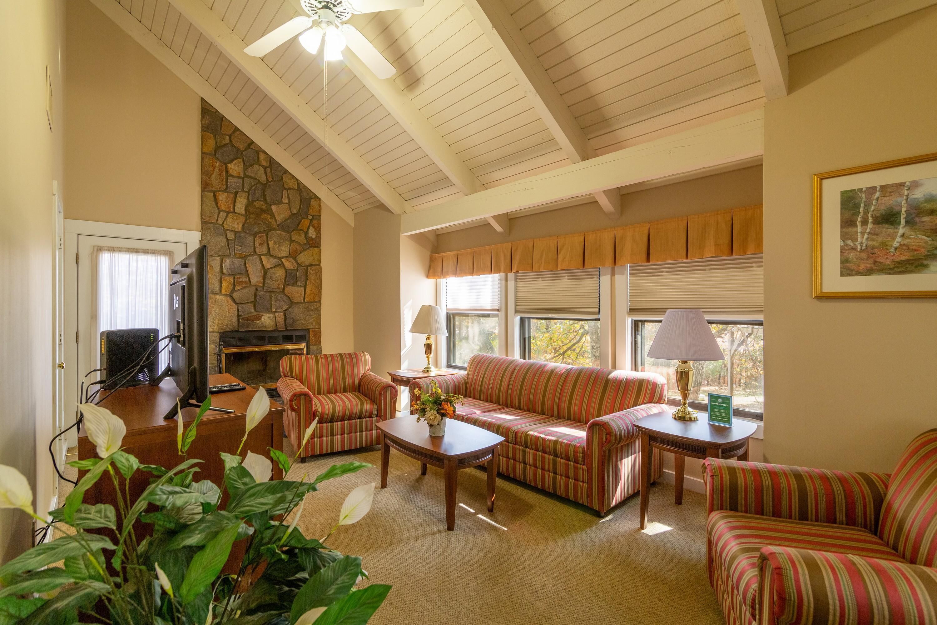 A cozy living room with striped sofas, a stone fireplace, and a ceiling fan.