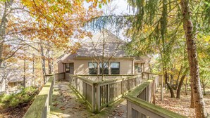 A wooden deck leading to a house surrounded by trees with autumn leaves.