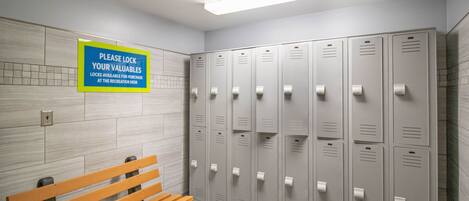 A locker room with multiple lockers, a bench, and a sign instructing to lock valuables.