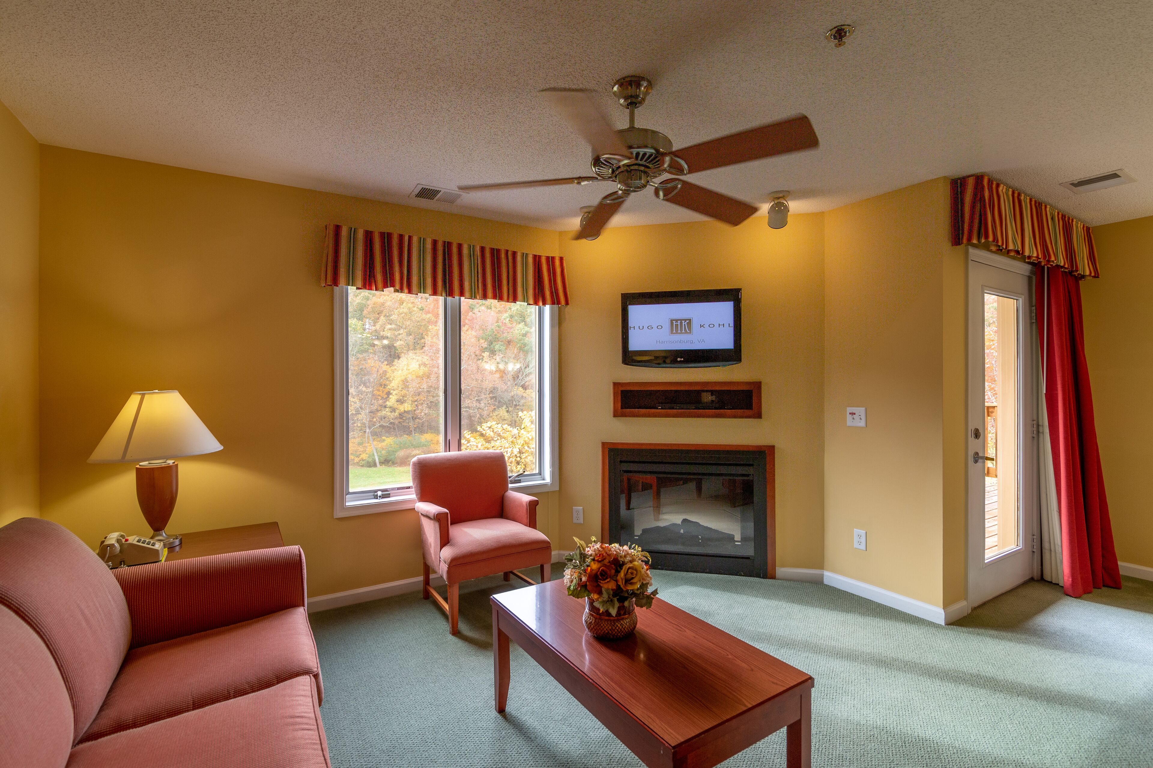 A living room with a sofa, armchair, coffee table, fireplace, television, and a ceiling fan.