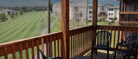 A wooden deck with chairs overlooking a well-maintained lawn and a mountain backdrop.