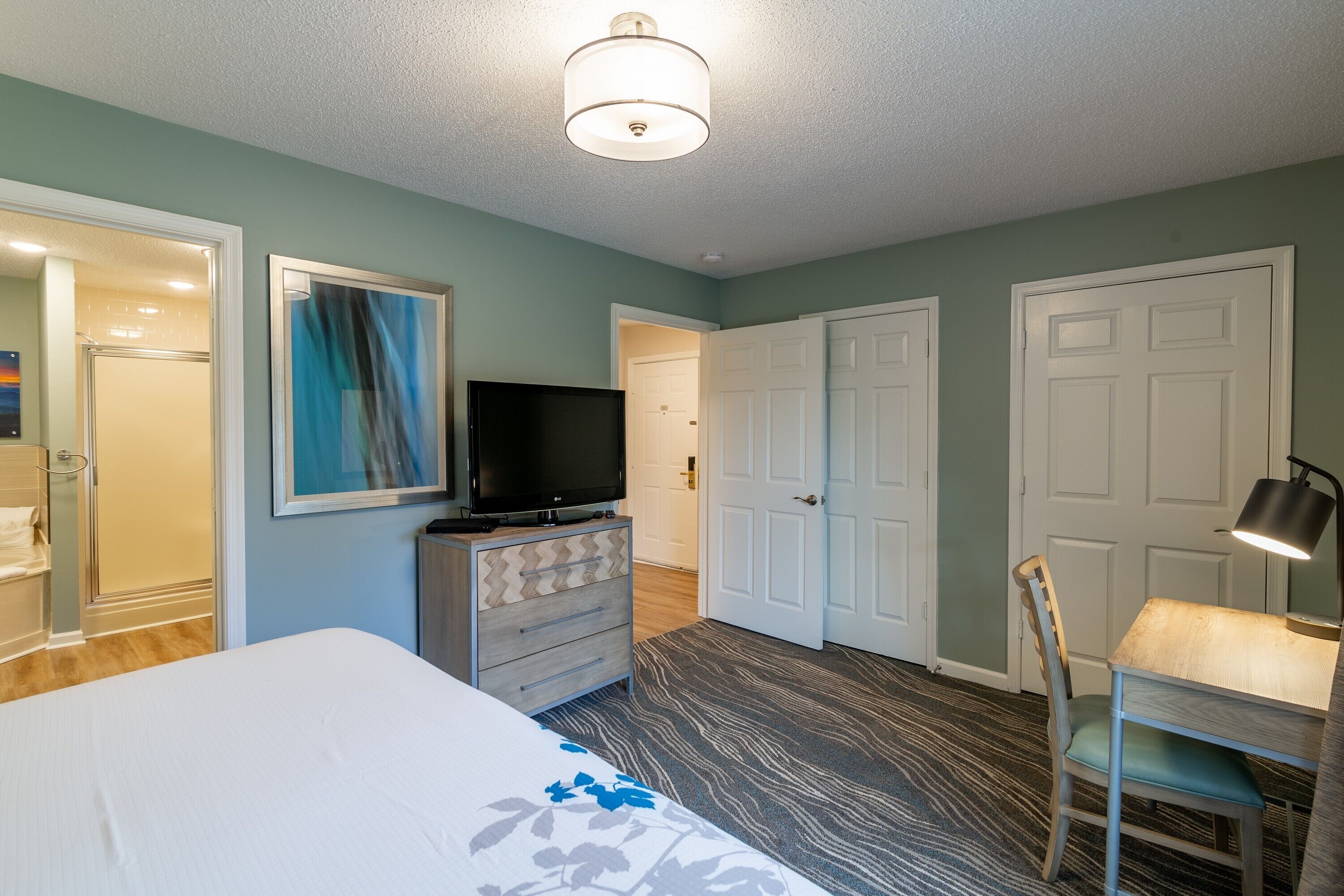 A bedroom with a bed, a dresser, a television, and a desk with a chair.