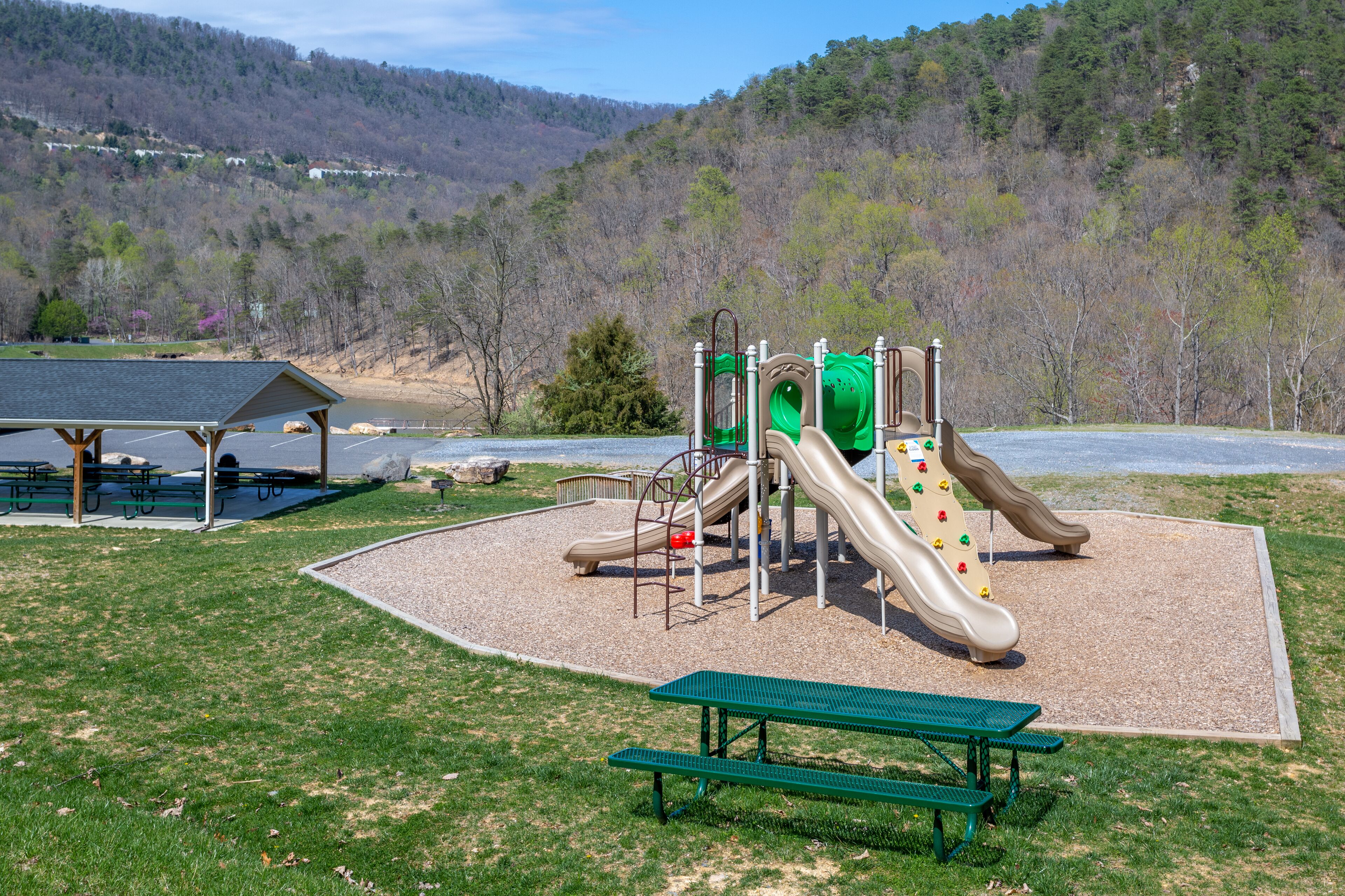 Un parque infantil con toboganes y estructuras de escalada, rodeado de una zona de picnic y bancos.