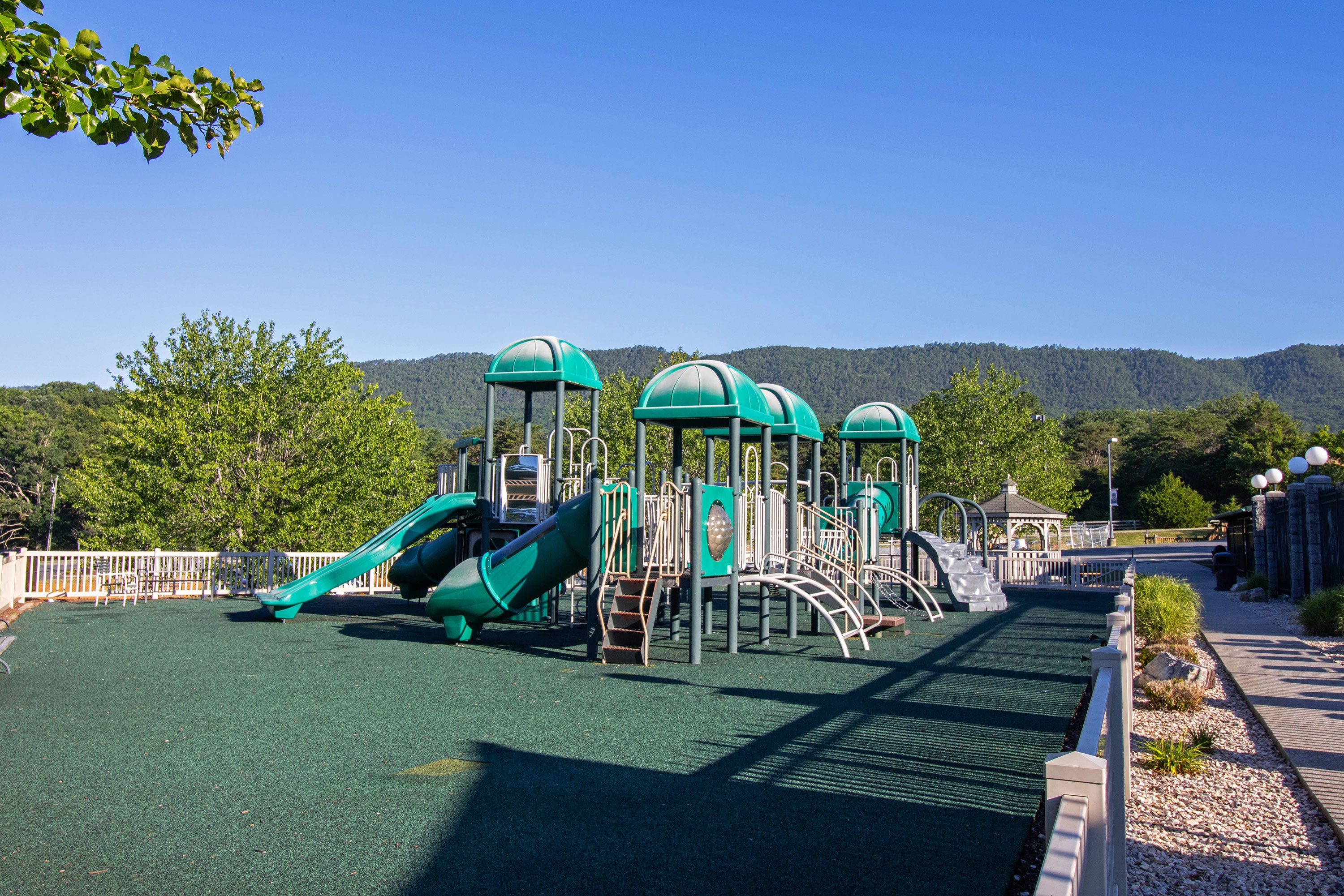 Un parque infantil con toboganes y estructuras para escalar, rodeado de una valla y árboles.