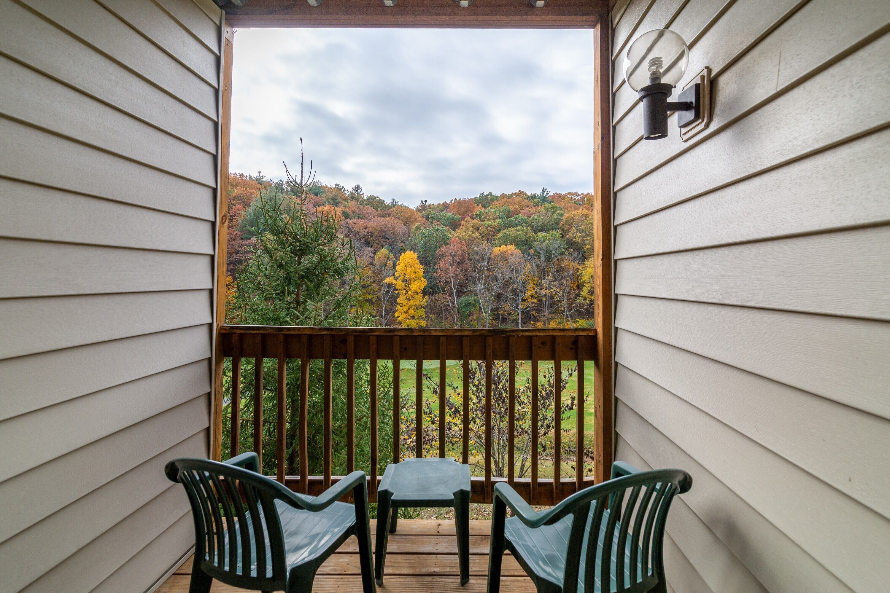 Une terrasse en bois avec deux chaises et une petite table, donnant sur une zone boisée aux couleurs automnales.