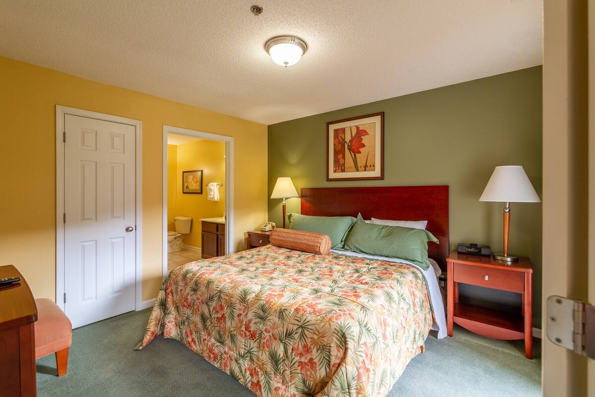Habitación de hotel con una cama, mesitas de noche, una puerta y un cuadro en la pared.