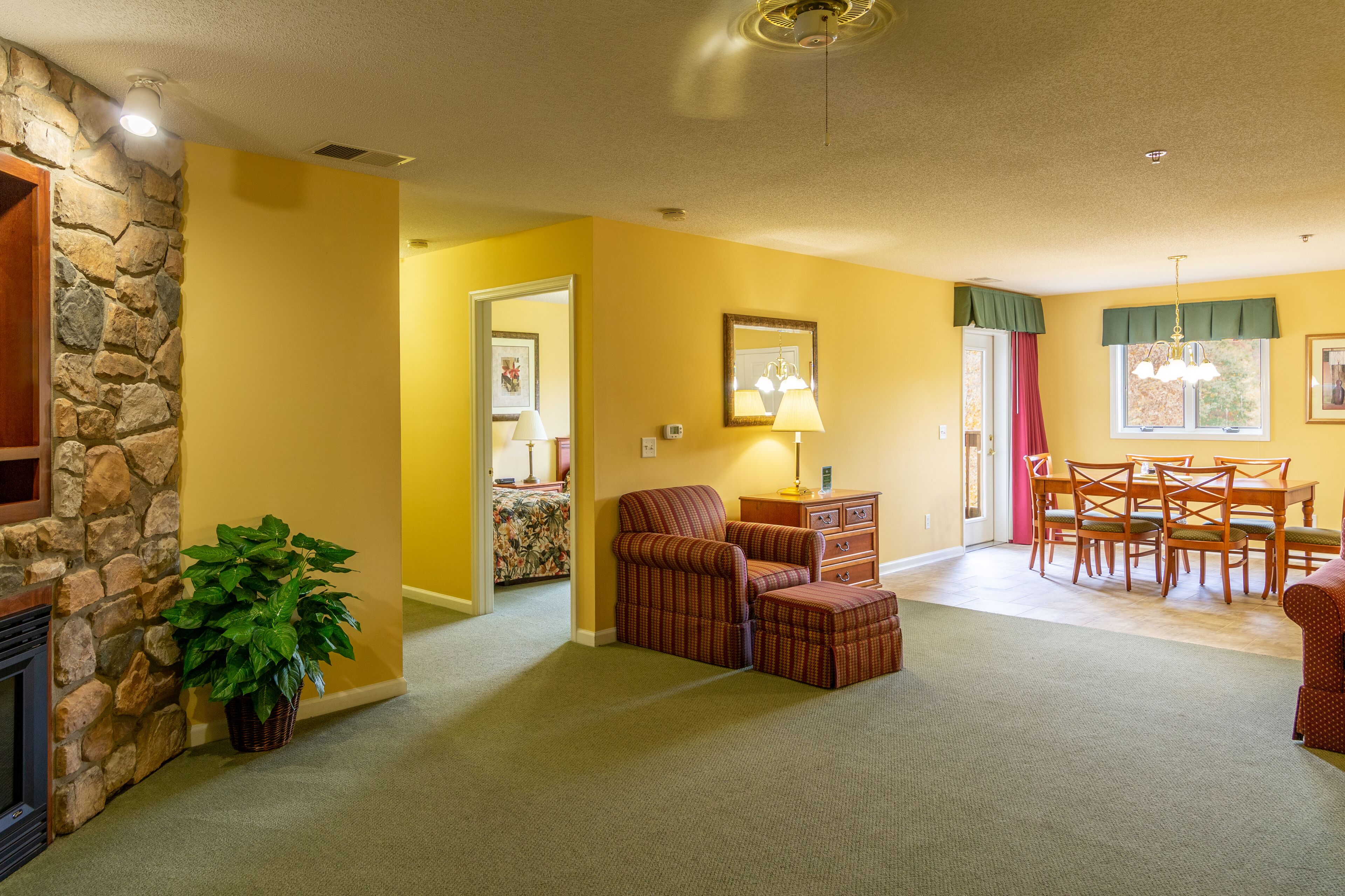 A living room with a stone fireplace, a dining area with a table and chairs, and a cozy seating area with a chair and ottoman.