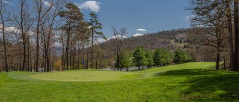 A golf course with a clear sky, trees, and a distant building.