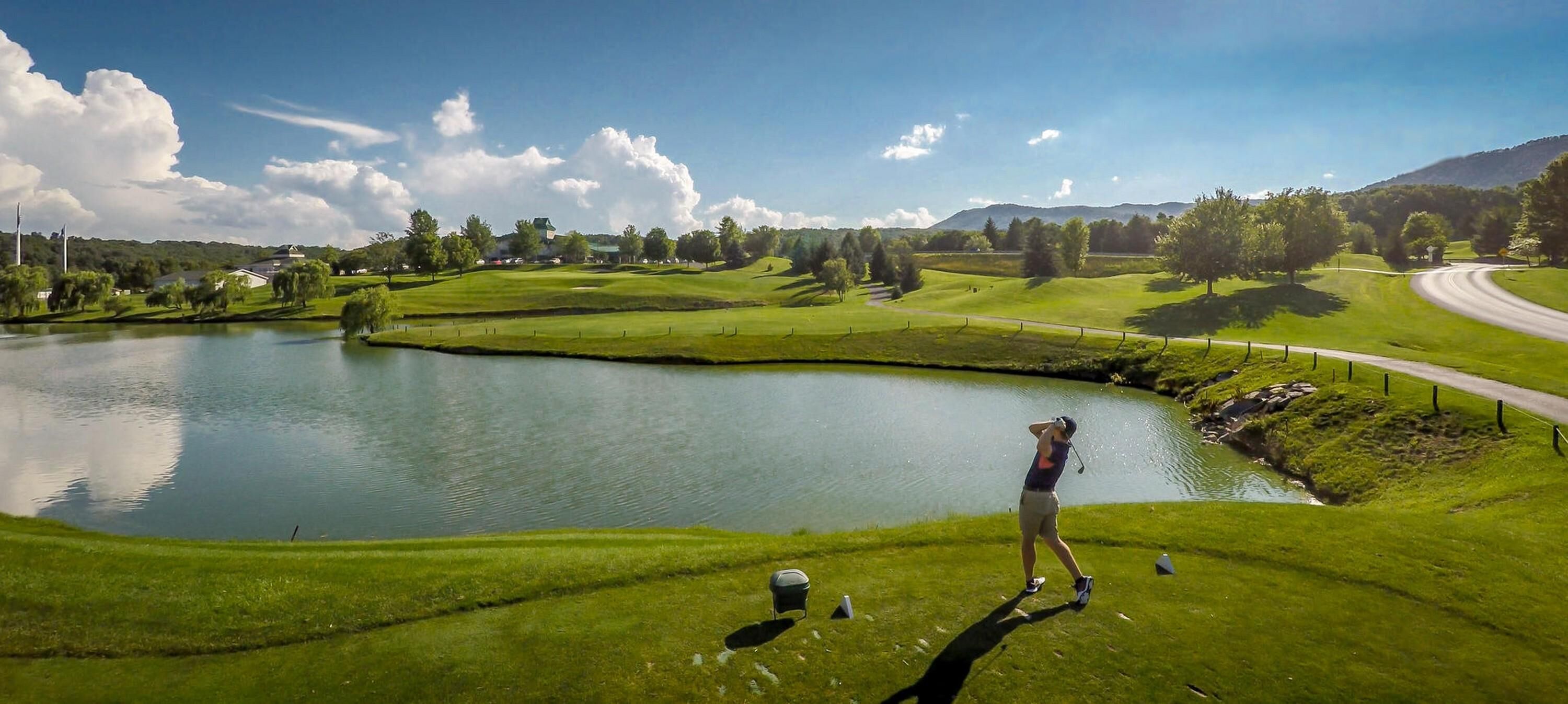 Un terrain de golf avec un étang, une route et un bâtiment en arrière-plan.