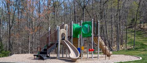 A playground with slides and climbing structures surrounded by a gravel area and trees.