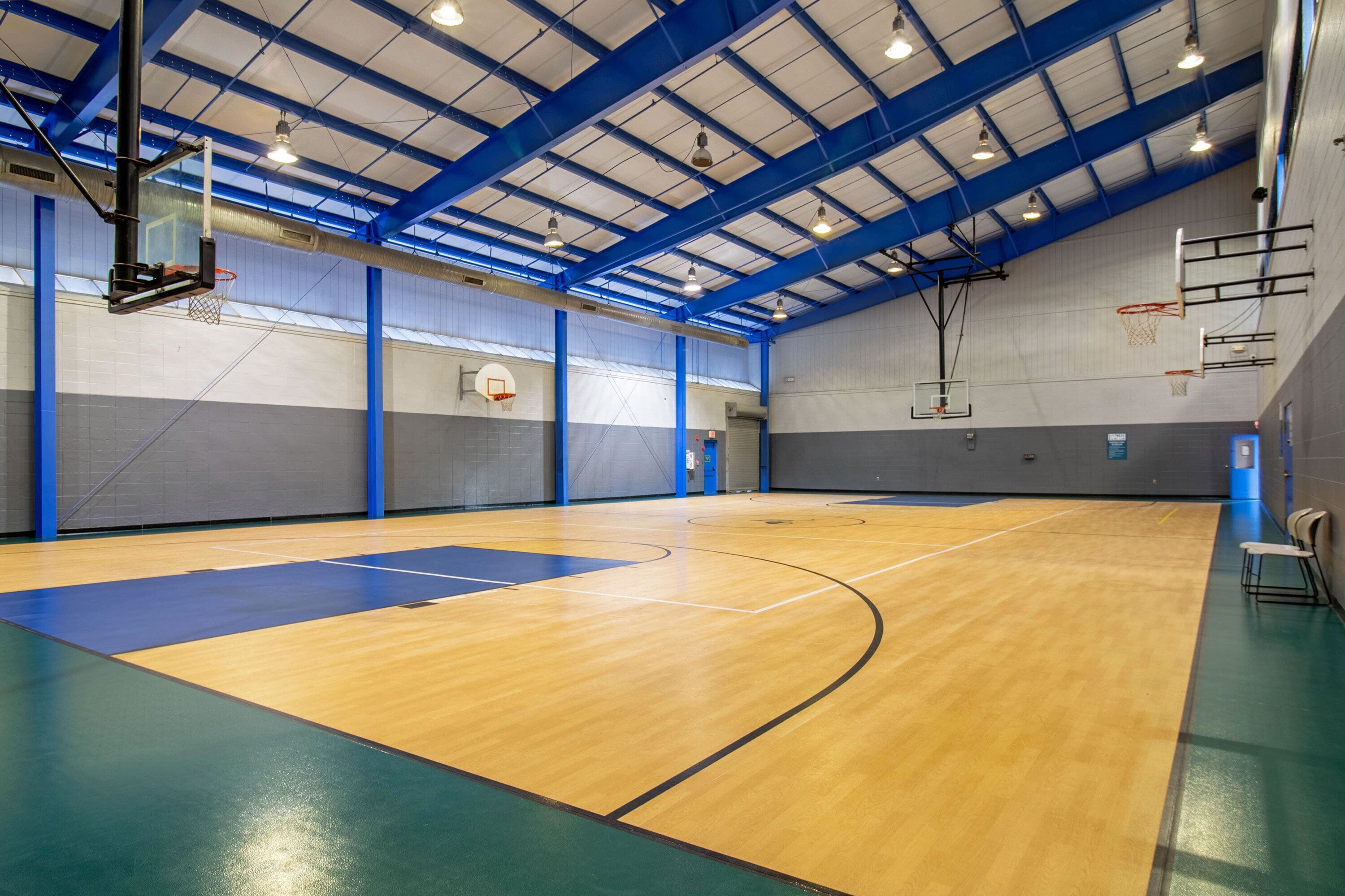 An indoor basketball court with blue and grey walls, a wooden floor, and multiple basketball hoops.