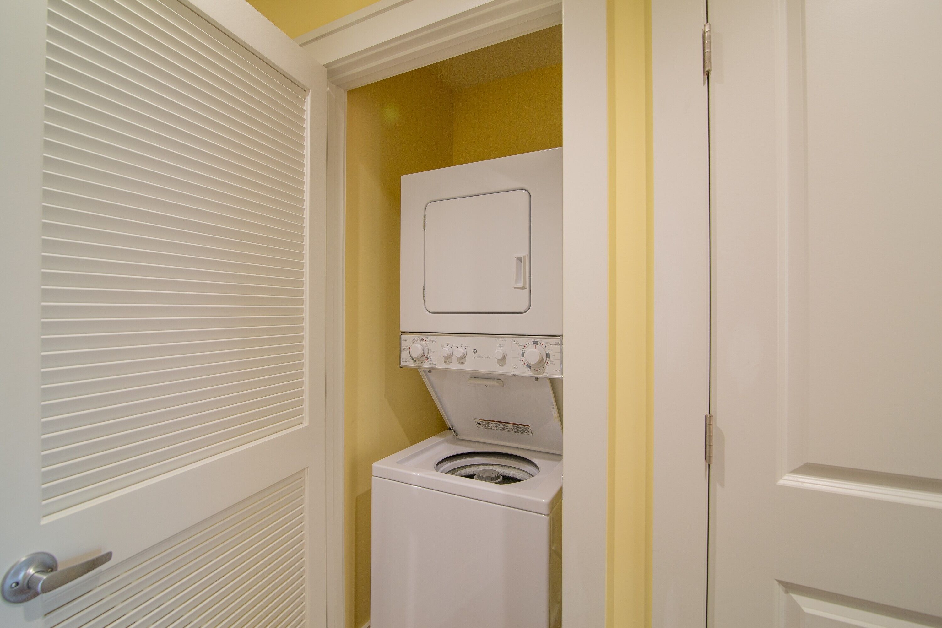 A compact laundry room with a front-loading washer and dryer, a door with a handle, and a yellow wall.