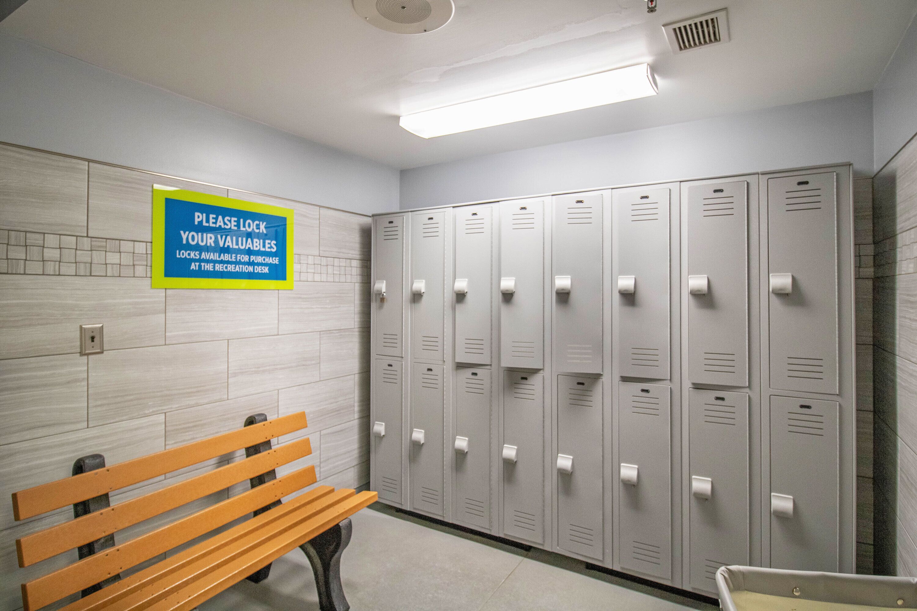 A locker room with multiple lockers, a bench, and a sign instructing to lock valuables.