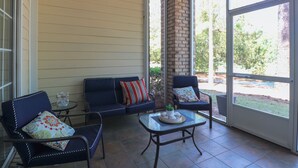 Eine sonnendurchflutete Terrasse mit einer Couch, zwei Stühlen, einem kleinen Tisch und einer Ziegelstütze.