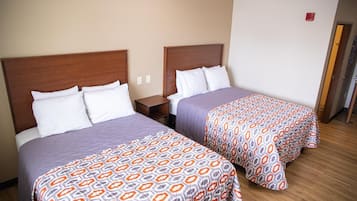 A hotel room with two beds, each with a wooden headboard, white pillows, and patterned bedspreads.