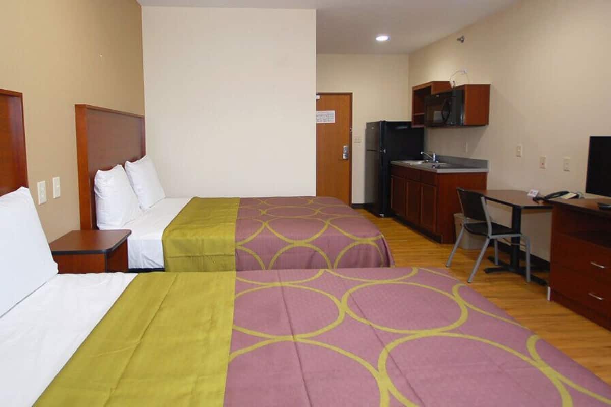 A hotel room with two beds, a desk, a chair, a television, and a kitchenette.