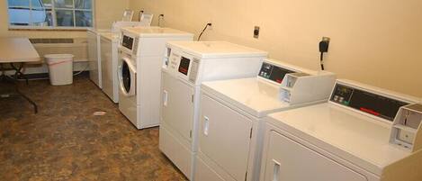 A laundry room with four white washing machines and a table with a chair.
