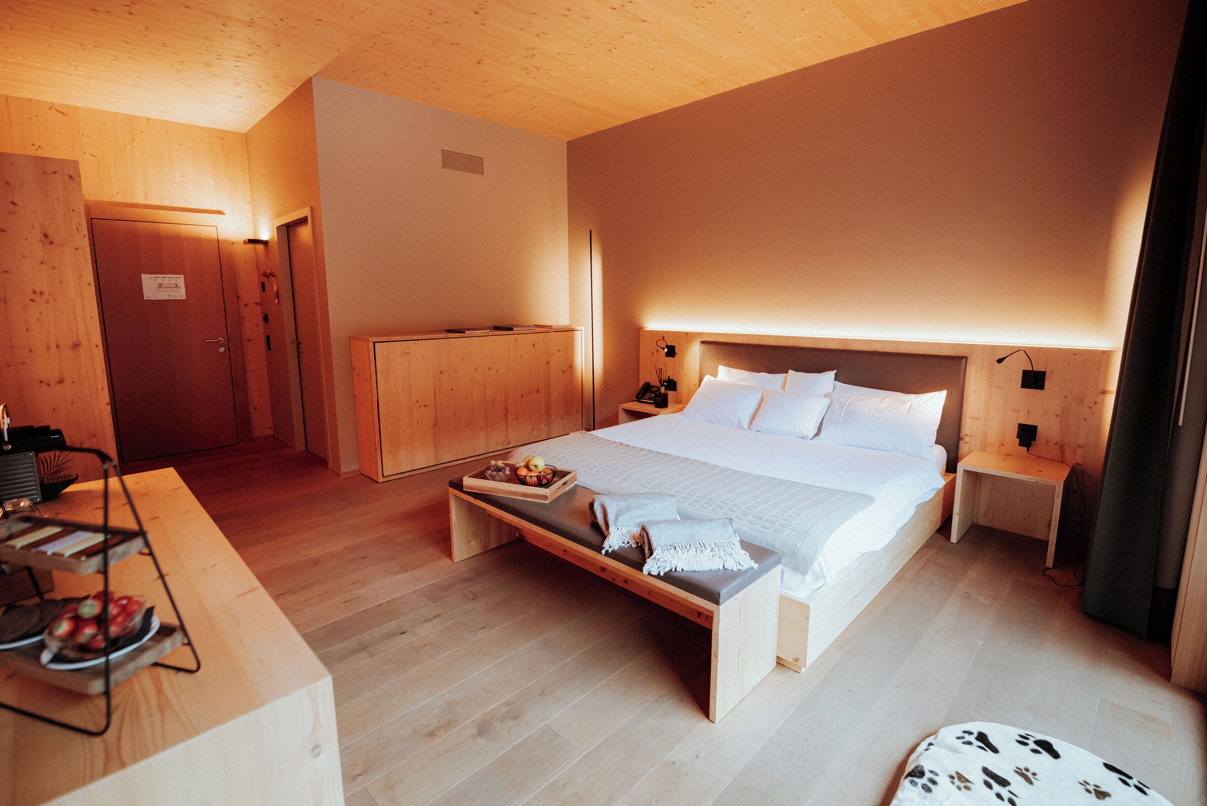Un dormitorio con suelo de madera, una cama, mesitas de noche y un banco con una bandeja de comida.