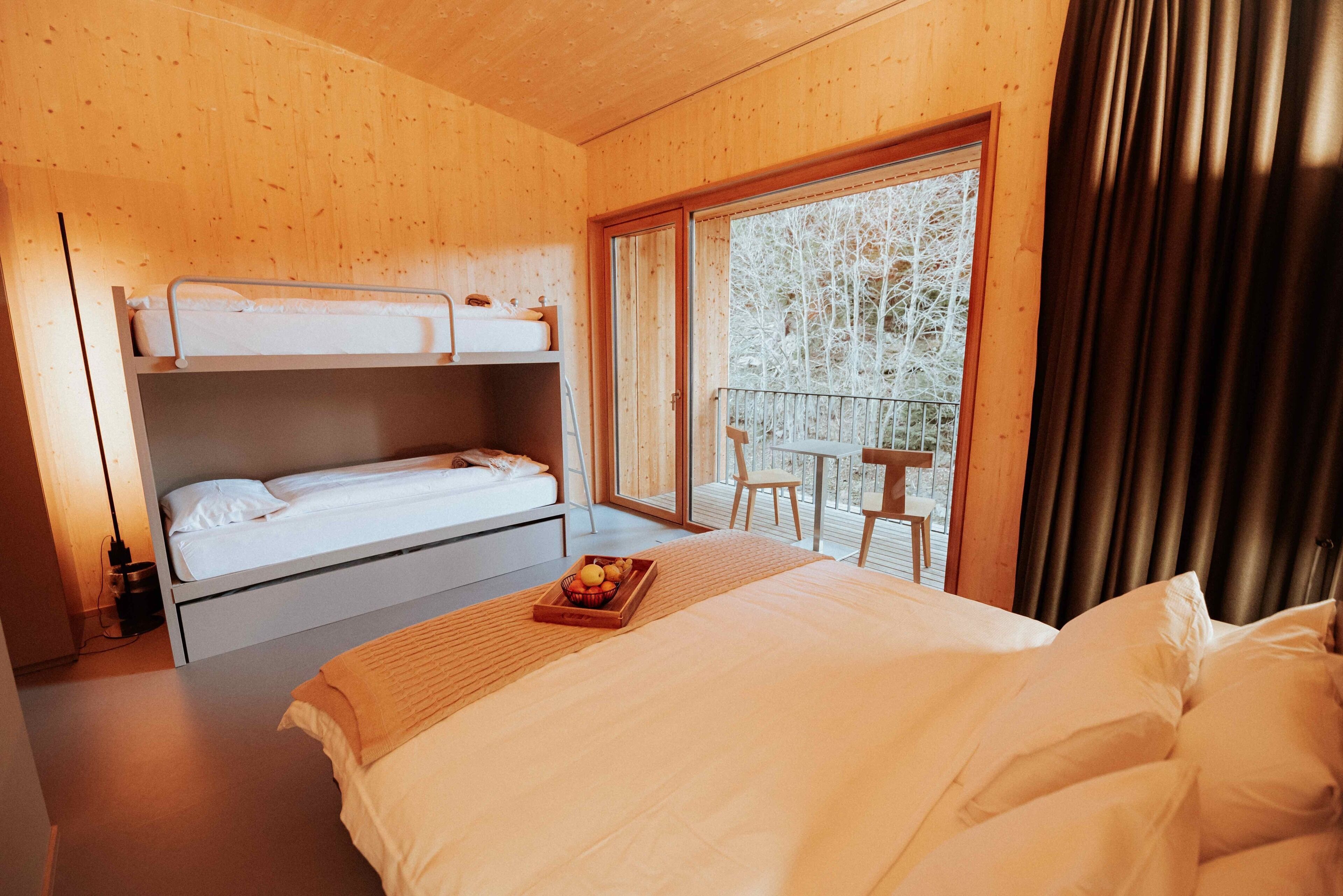Een slaapkamer met een stapelbed, een nachtkastje met een schaal fruit, en een balkon met een tafel en stoelen.