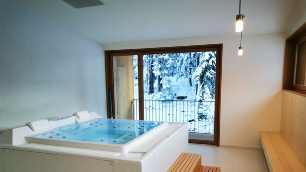 A modern bathroom with a large bathtub, a wooden bench, and a view of a snowy balcony. - Campra Alpine Lodge & Spa (Blenio)