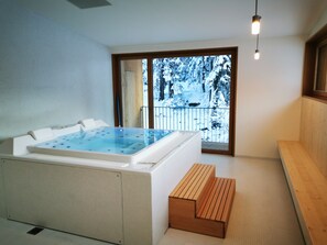 A modern bathroom with a large bathtub, a wooden bench, and a view of a snowy balcony. - Campra Alpine Lodge & Spa (Blenio)