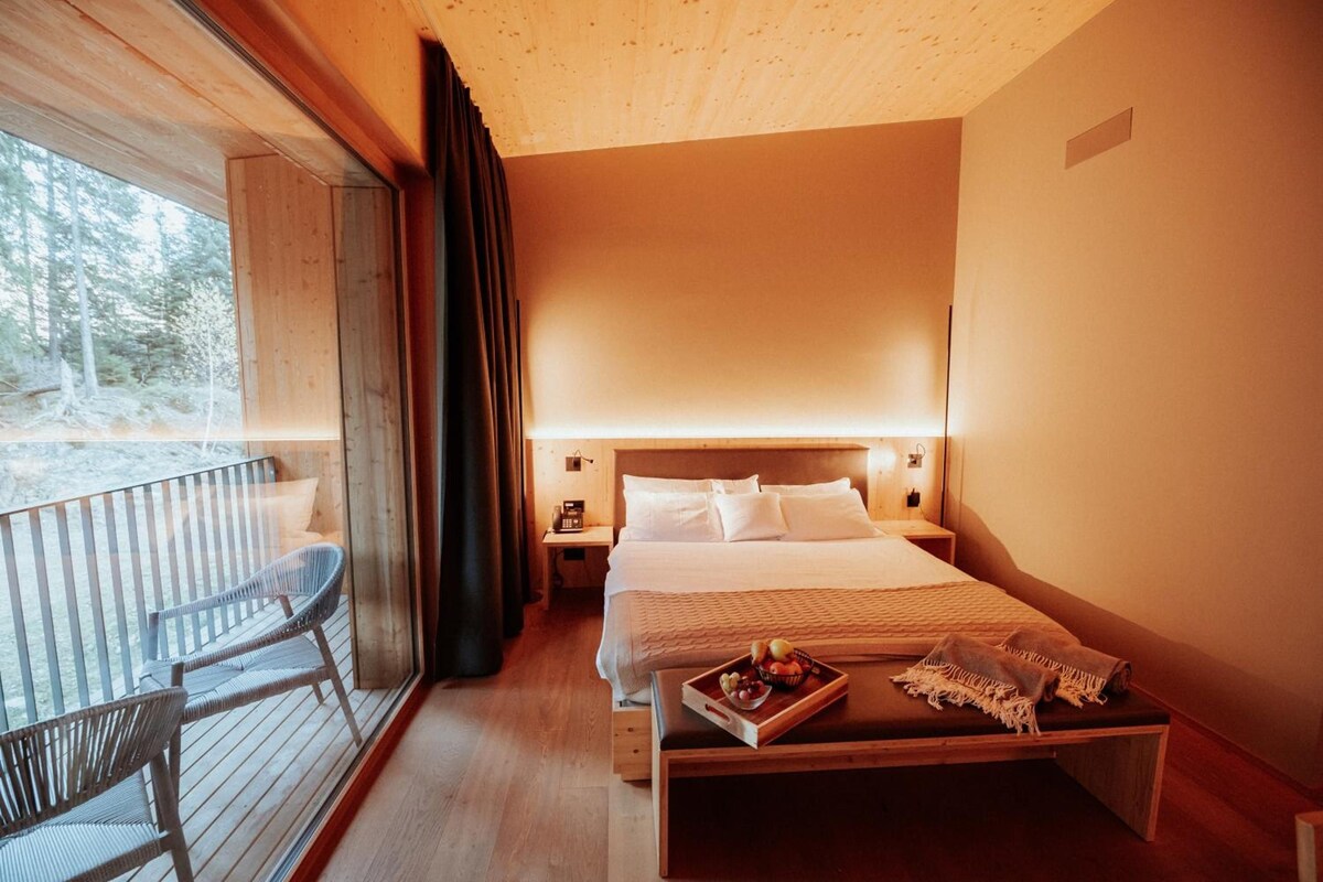 A hotel room with a bed, bedside table, and a balcony with a chair.