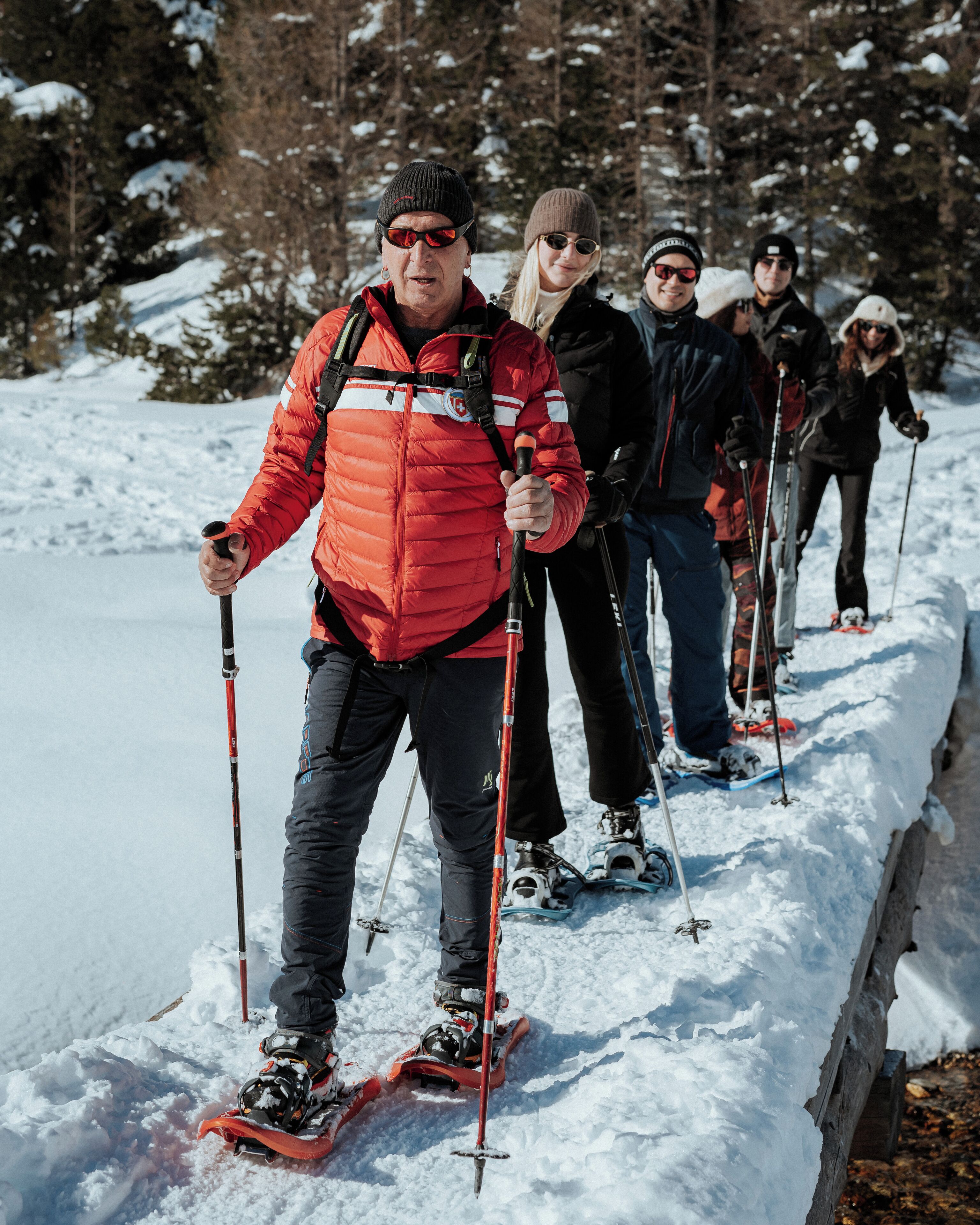 Un groupe de personnes pratique le ski de fond sur une piste enneigée, avec des arbres en arrière-plan.