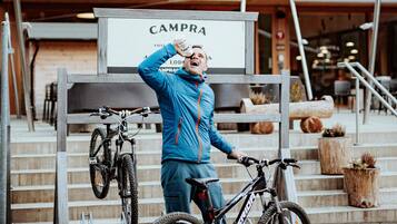 Una persona con una chaqueta azul parada junto a una bicicleta frente a un edificio con un letrero que dice "CAMPA".