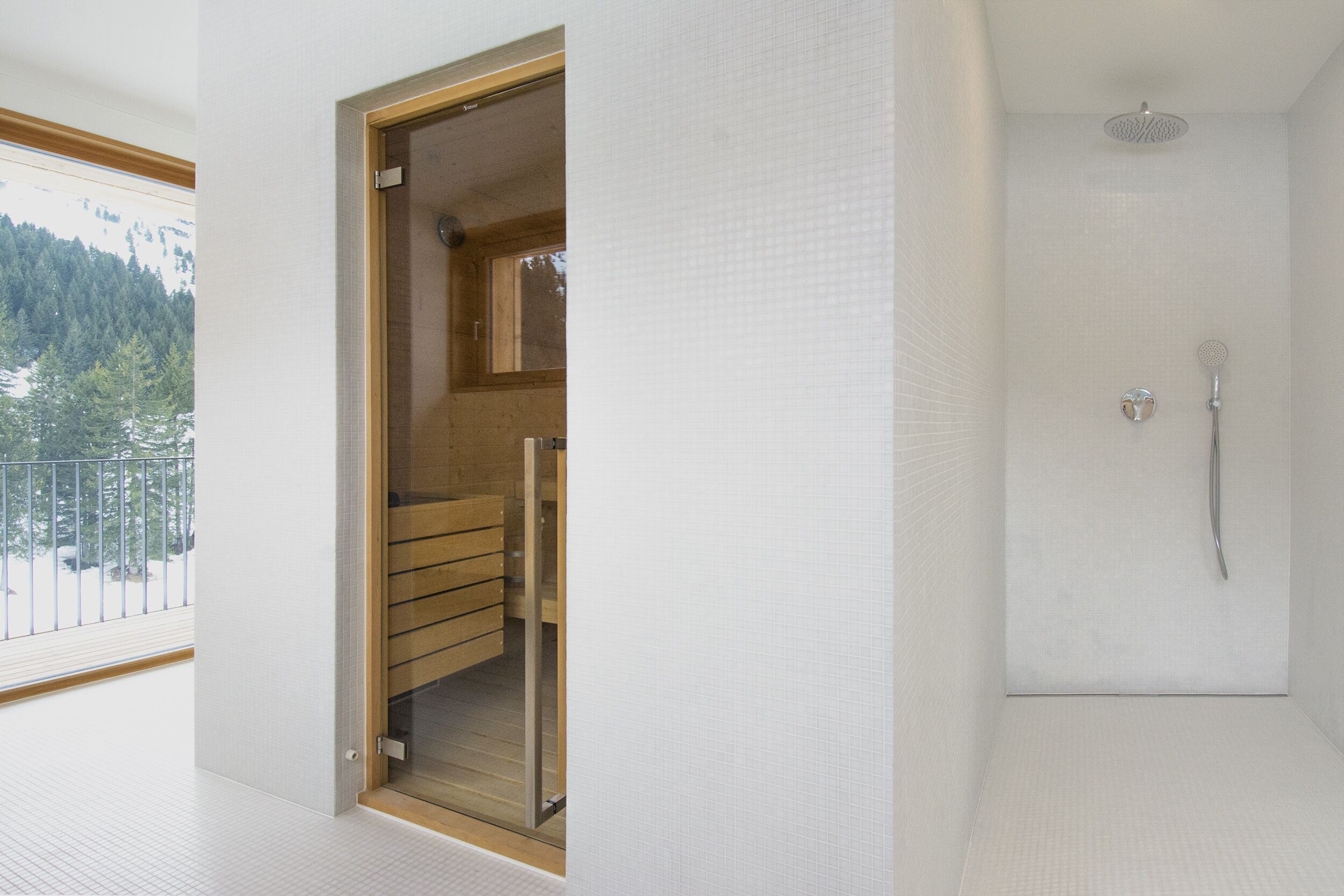 Ein modernes Badezimmer mit Dusche, einer Holzbank und Blick auf eine verschneite Landschaft durch ein Fenster.
