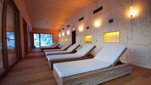 A row of wooden-framed sunbeds with white mattresses in a room with wooden walls and ceiling, and small wall-mounted lights. - Campra Alpine Lodge & Spa (Blenio)