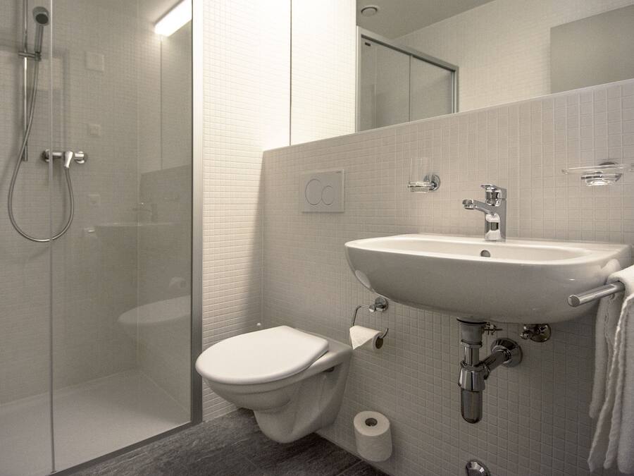 Un baño moderno con ducha de vidrio, inodoro blanco y lavamanos con barra para toallas.