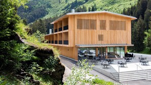 A modern wooden building with a terrace, surrounded by lush greenery and mountains. - Campra Alpine Lodge & Spa (Blenio)